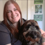 Jenn posing with her dog, with three photos on the wall behind her.