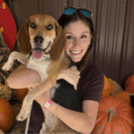 Photo of Jocelyn holding her dog and posed on top of pumpkins.